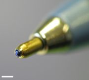 A ponta de uma caneta esferográfica descartável comum. A bola, com tinta azul sobre ela, pode ser visto. A barra de escala branca é 1 milímetro de largura.