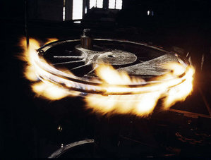 Pneu na roda de aço de condução de um locomotiva a vapor é aquecida com chamas de gás para expandir e soltá-lo para que ele possa ser removido e substituído.