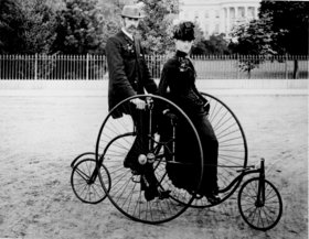 Esperta vestido casal sentado em uma bicicleta de 1886-modelo para dois.